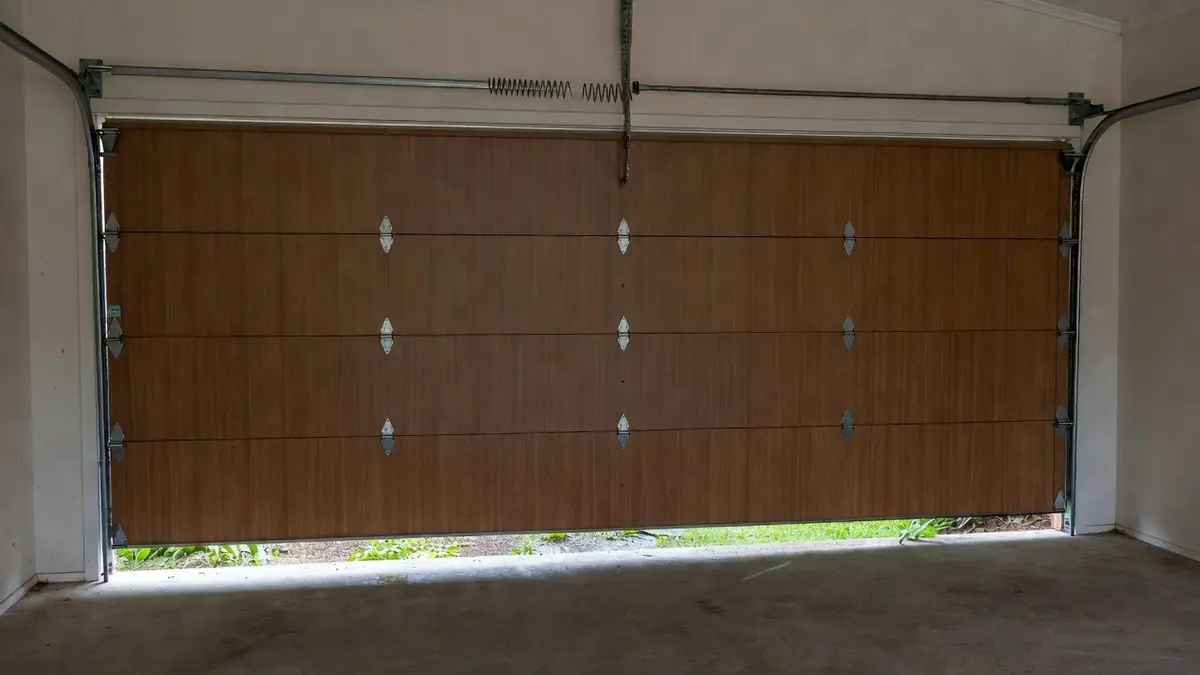 A sectional door stuck a short way open, with a broken torsion spring on the bar above